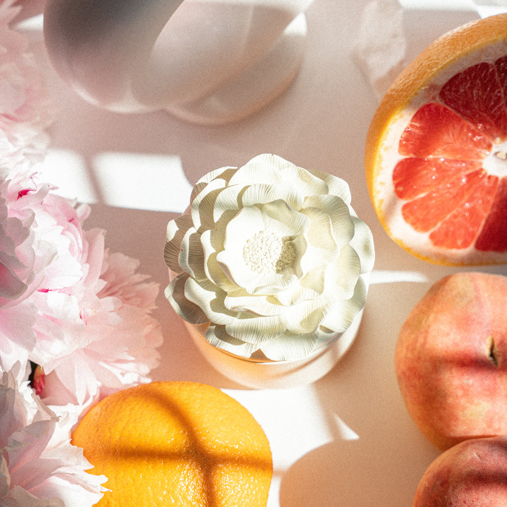 Flower-lidded white candle next to sliced grapefruit and orange