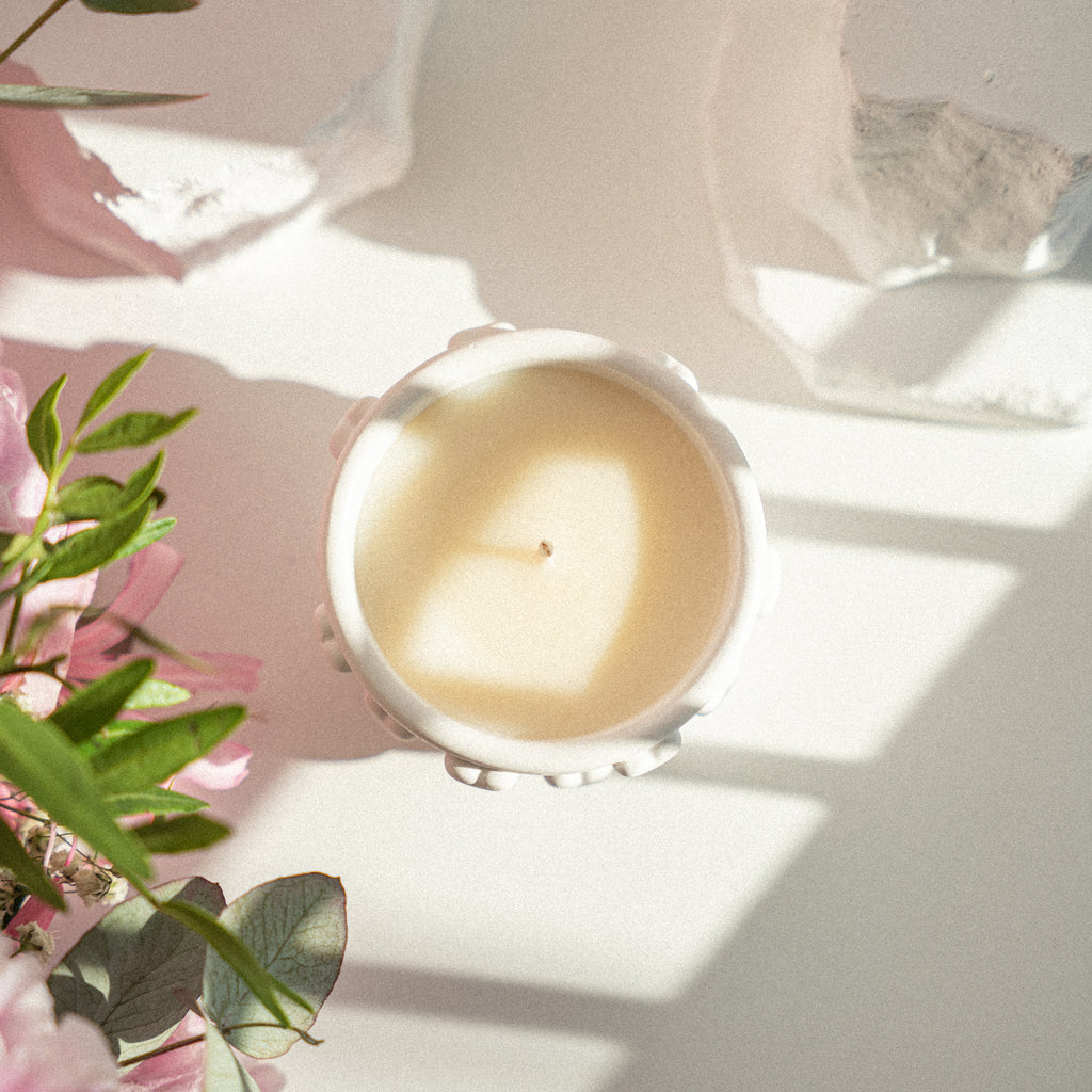 Top view of a handmade candle in a white artistic jar with 3D heart details, styled with flowers and soft natural light