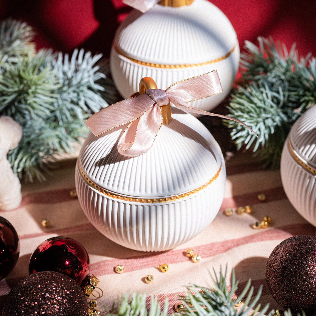 Christmas ornament-shaped candle with golden accents and pink ribbon